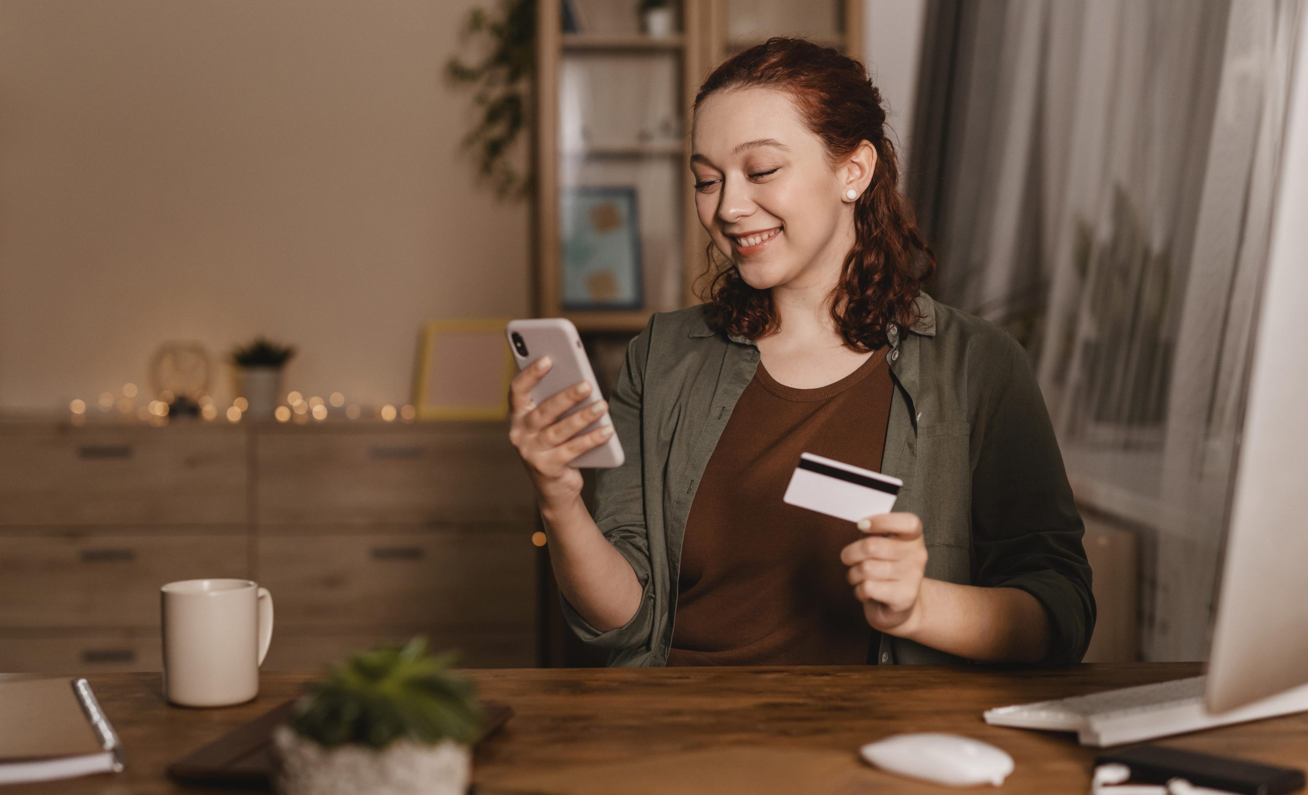 Smiley Woman Using Her Smartphone Home With Credit Card Scaled